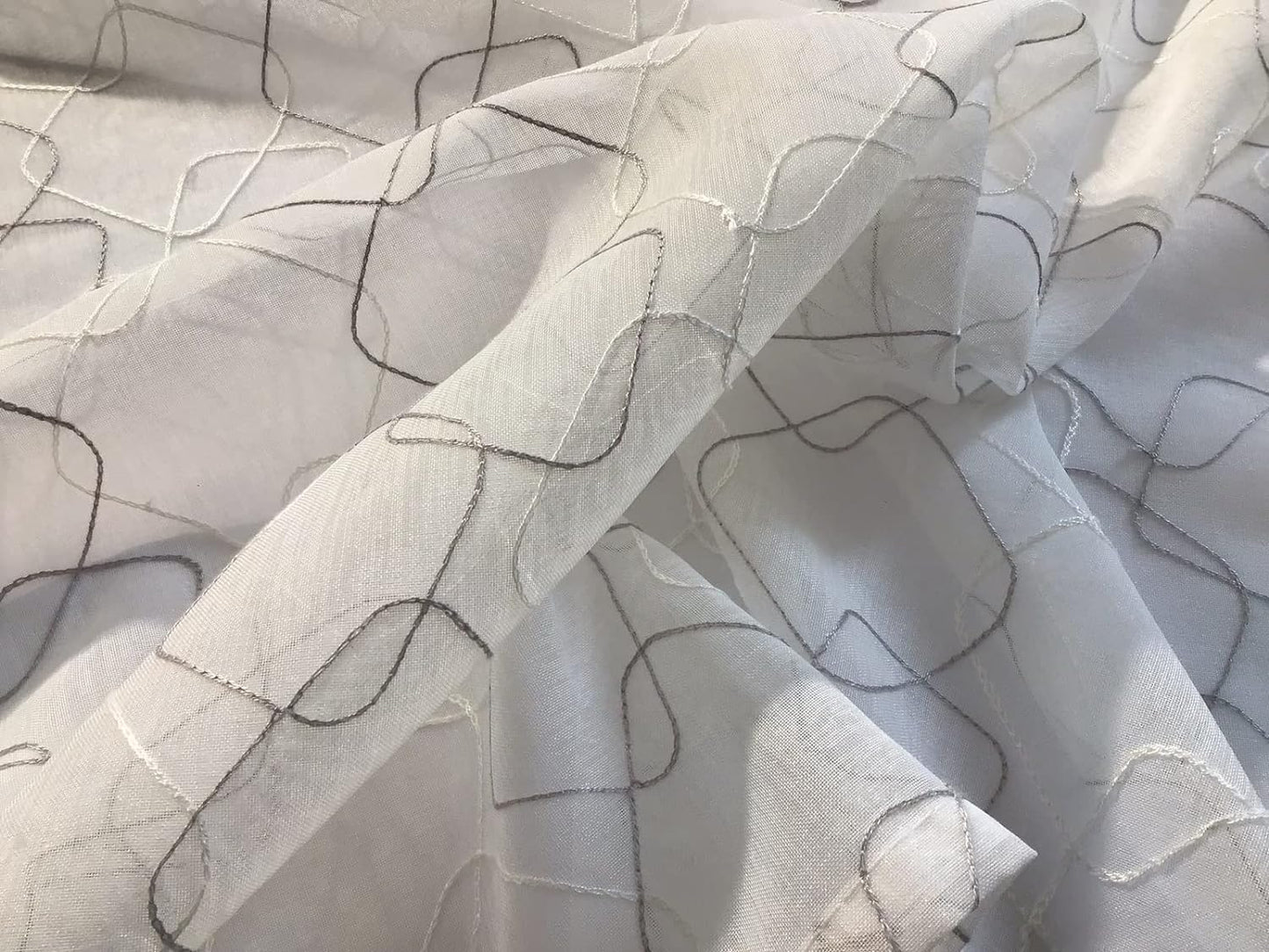 Dettaglio ravvicinato del tessuto della tenda a vetro bianca con ricamo geometrico bianco e grigio