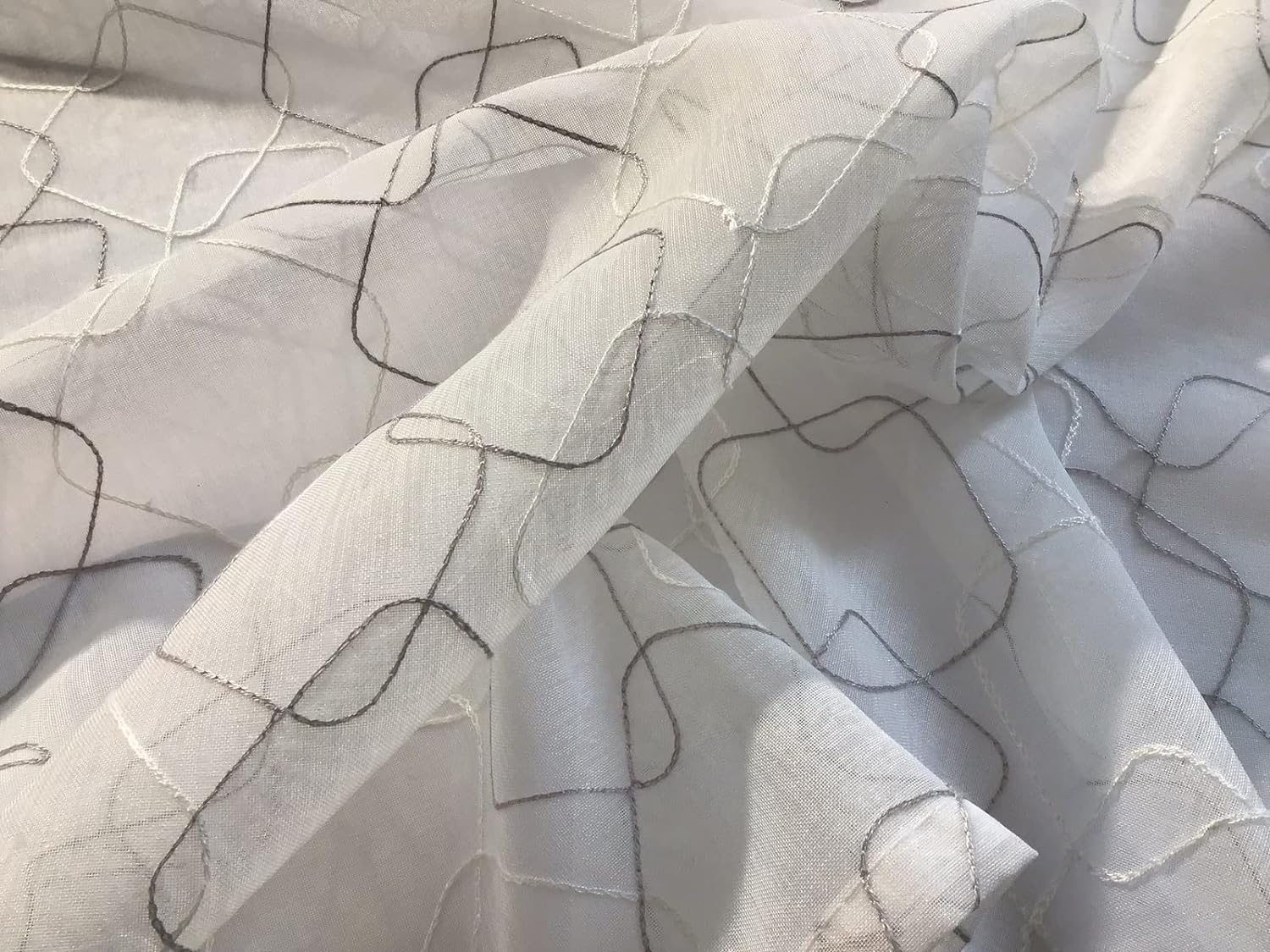 Dettaglio ravvicinato del tessuto della tenda a vetro bianca con ricamo geometrico bianco e grigio