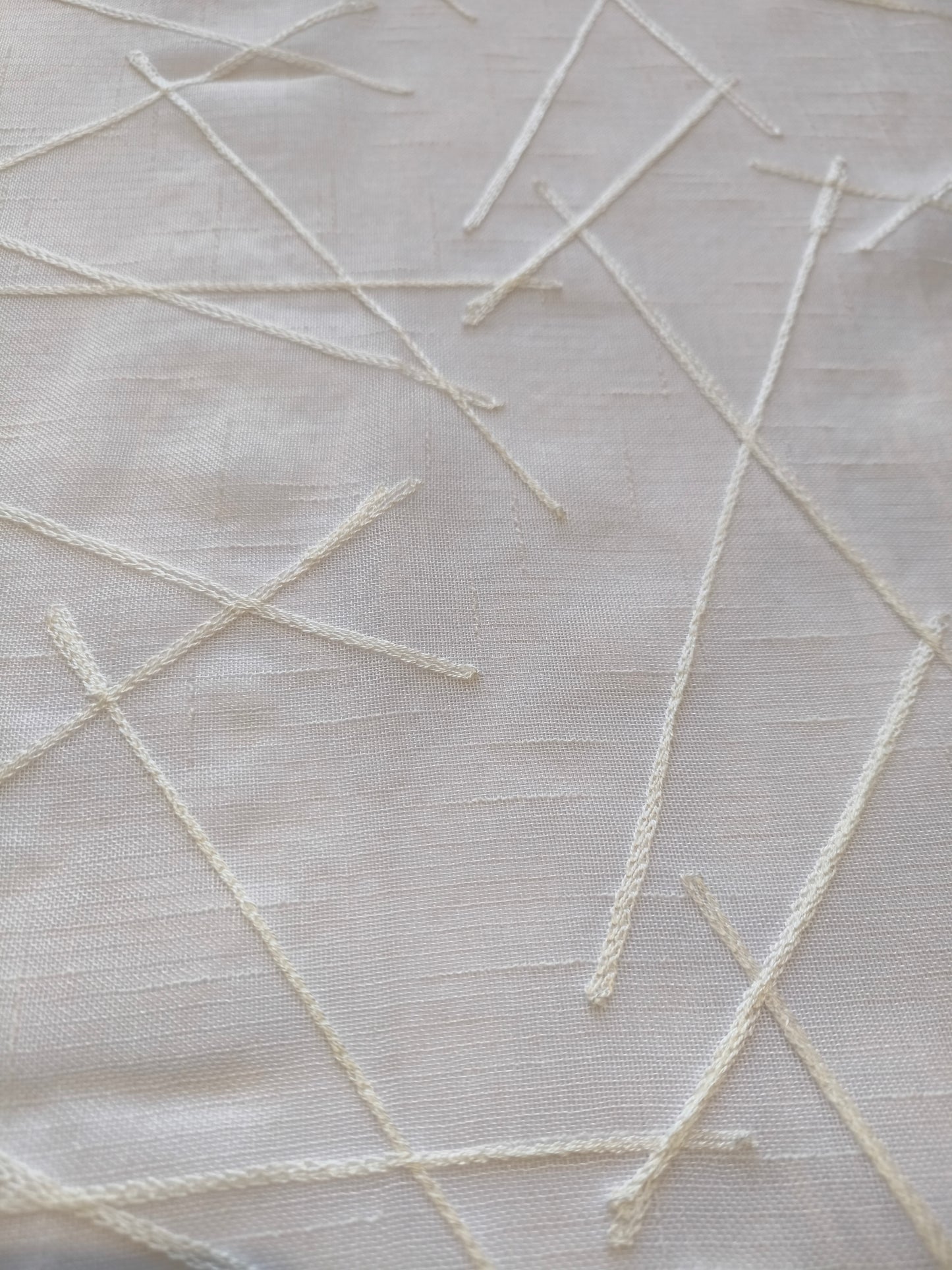 Dettaglio del ricamo bianco su tenda con disegno geometrico.