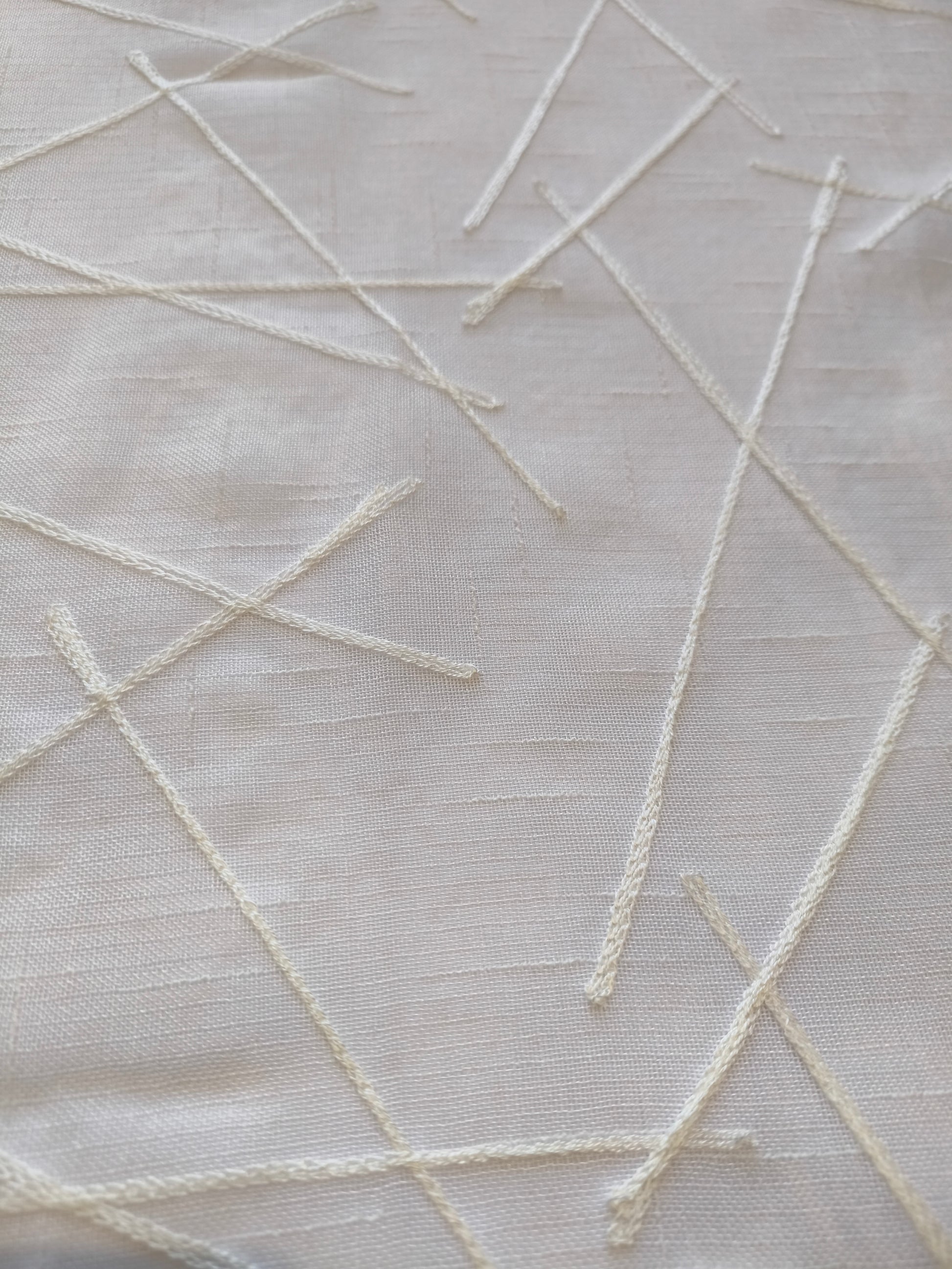 Dettaglio del ricamo bianco su tenda con disegno geometrico.