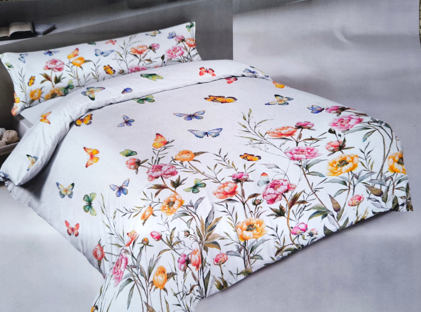 Foto del lenzuolo copriletto rose farfalle in 100% cotone, steso sul letto, che mostra la stampa digitale di rose gialle e rosa con farfalle e balza coordinata.