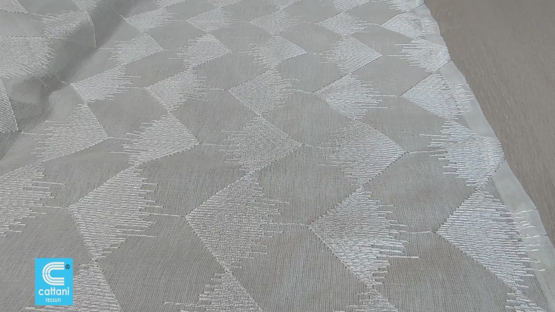 Il video mostra una panoramica del tessuto bianco con ricamo geometrico e spiega come arricciare la tenda per adattarla al binario. 