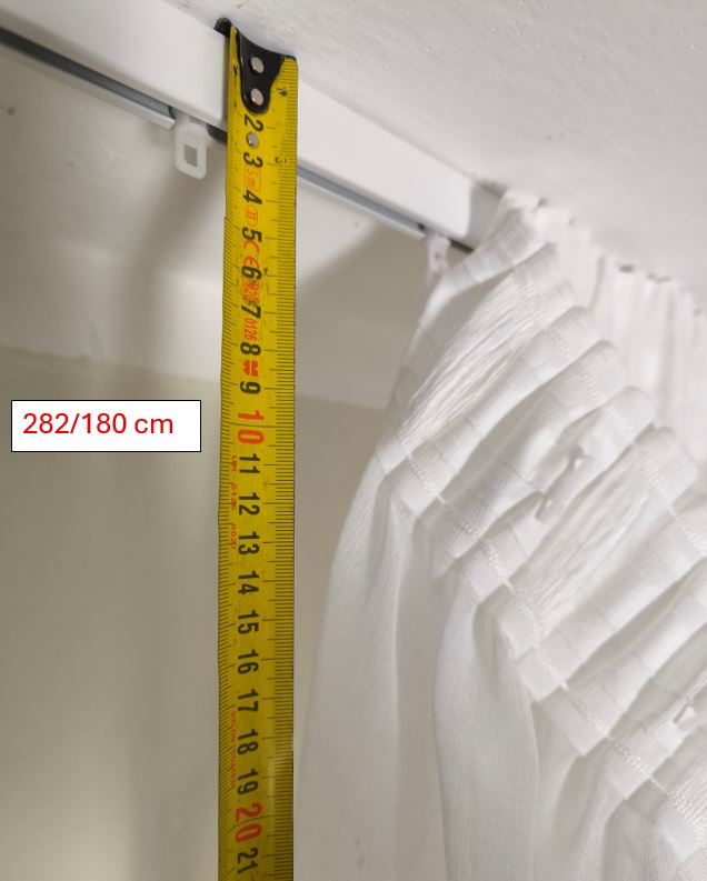 Dettaglio che mostra da dove prendere la misura per determinare l’altezza di una tenda con fettuccia arricciatende in tessuto ricamato a foglie in un salotto elegante.