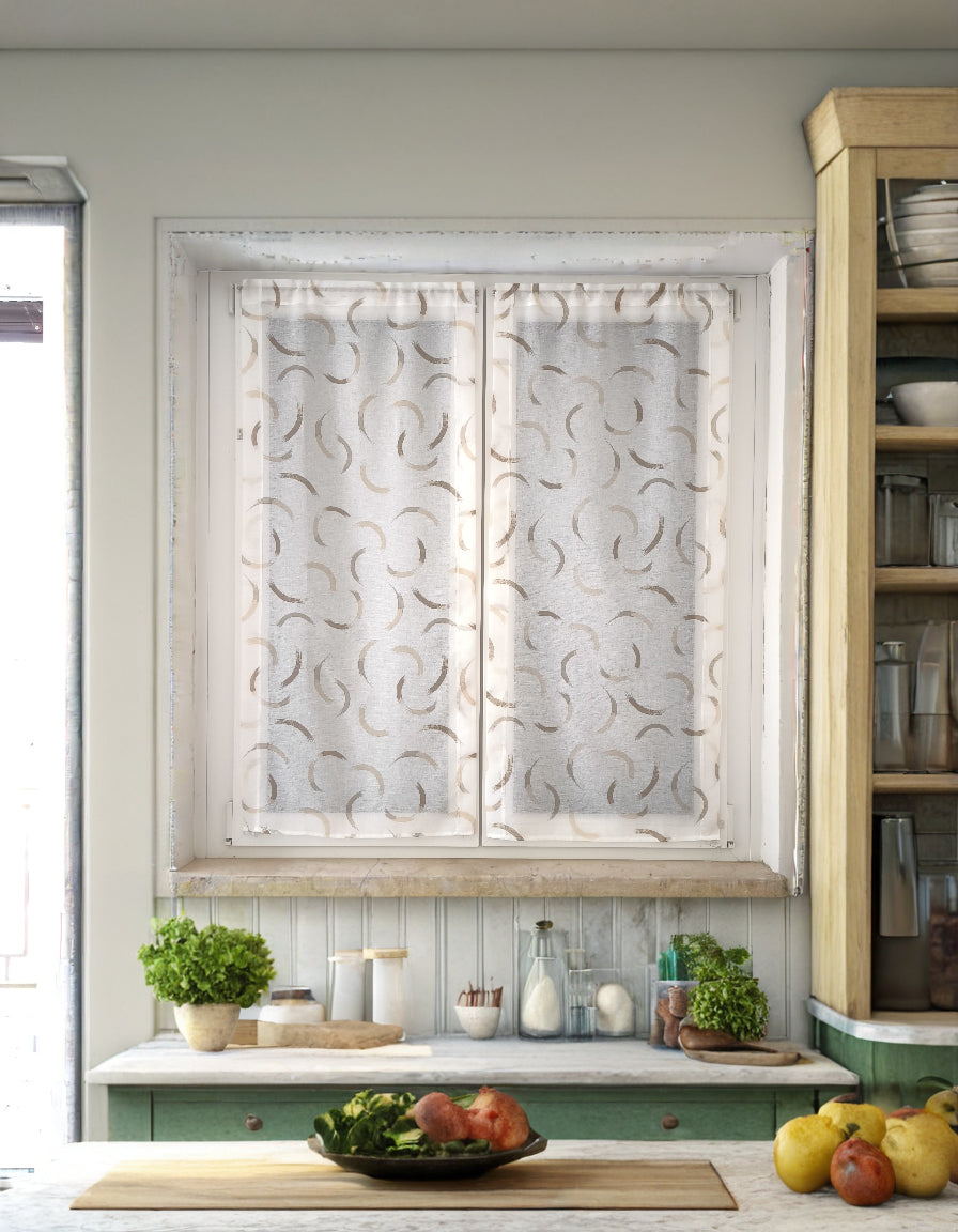 Coppia di tende a vetro con disegno effetto pennellate beige, appese a una finestra in una cucina