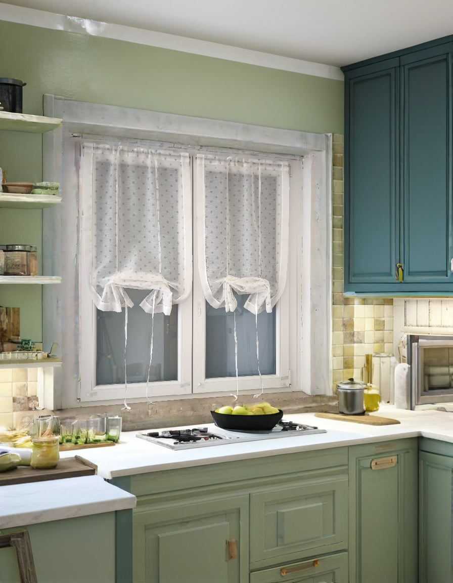 Una cucina con una finestra coperta da tende bianche con stampa a pois beige, regolate all’altezza desiderata per filtrare la luce naturale.
