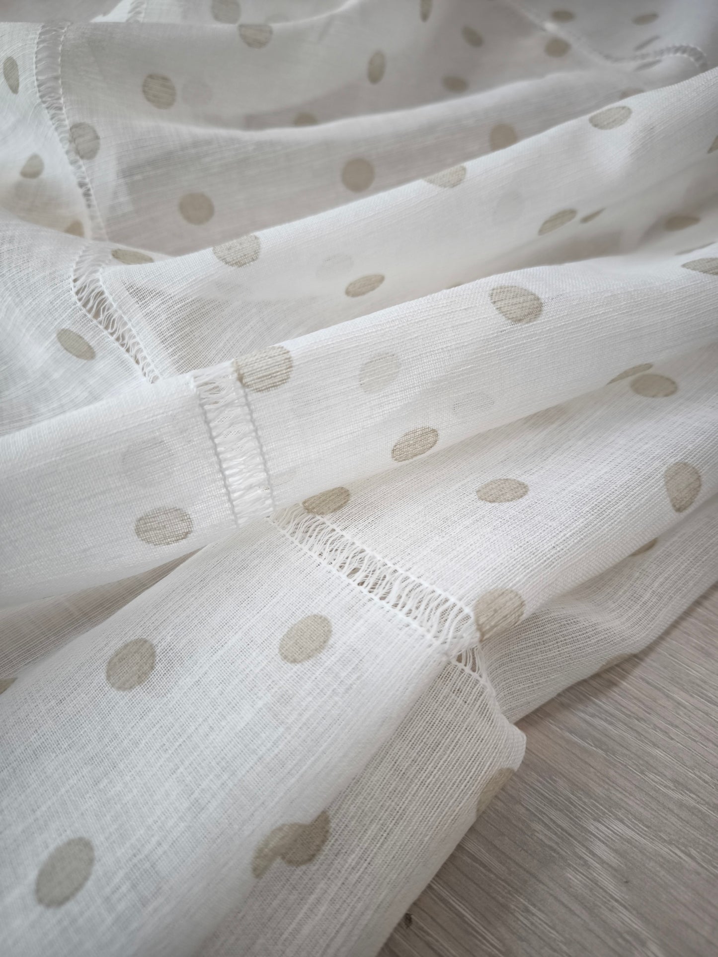 Primo piano del tessuto bianco della tenda con una stampa a pois beige distribuiti uniformemente.