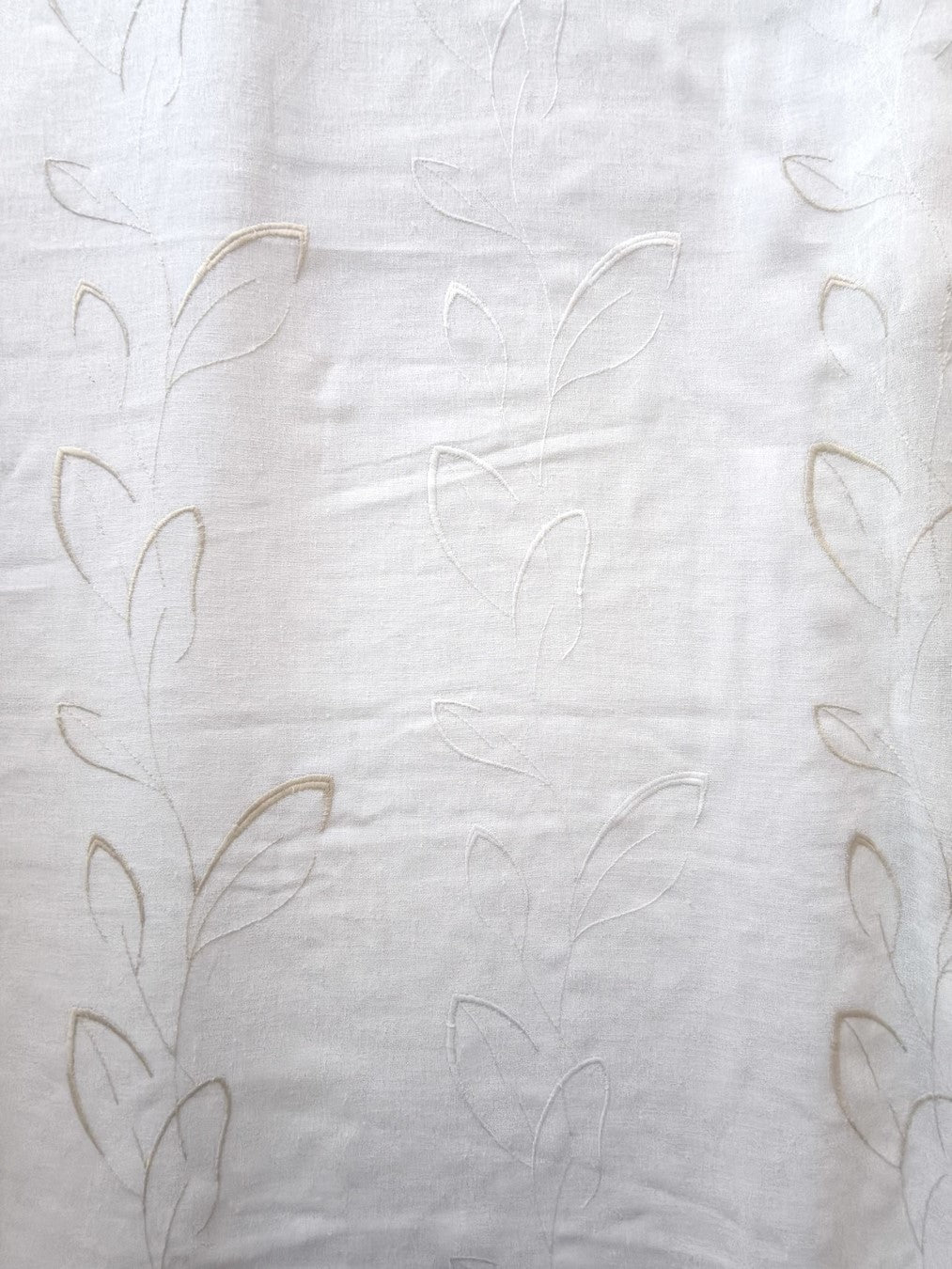 Dettaglio del ricamo raffigurante una foglia stilizzata bianca e beige.